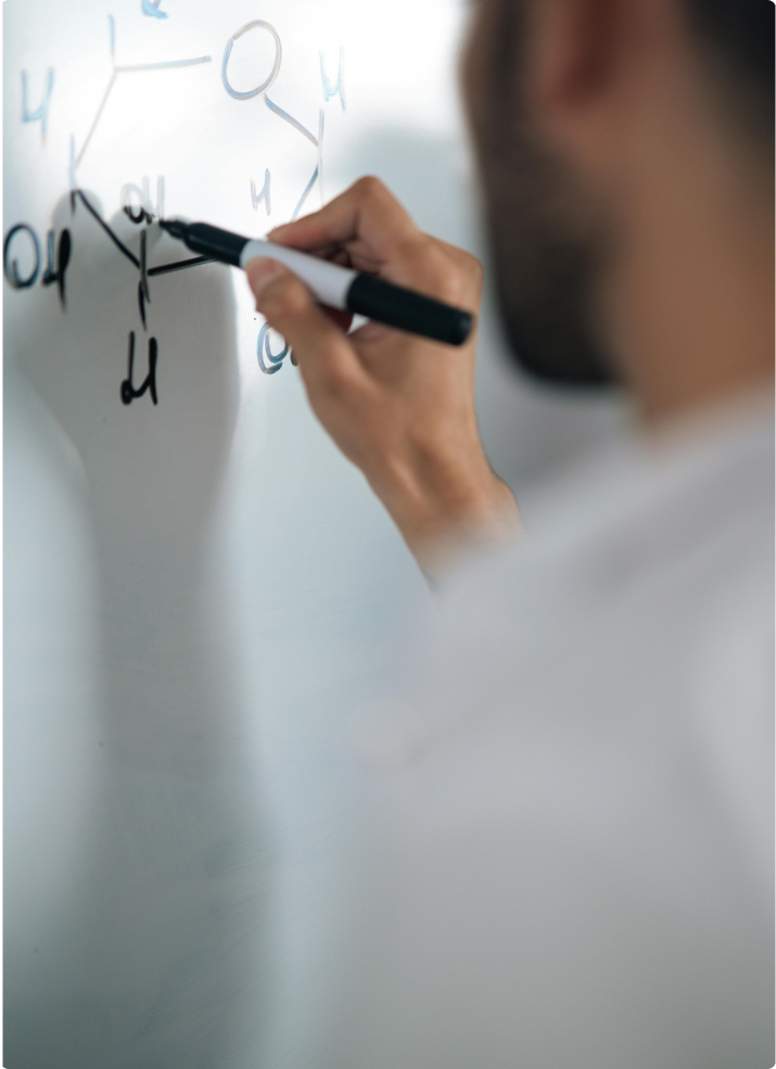 Close-up of a hand holding a marker, drawing a chemical or molecular structure diagram on a whiteboard